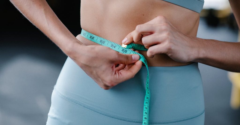 Close-up of a woman measuring her waist with a tape in a fitness setting.